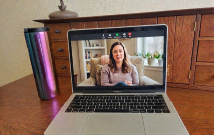 Laptop on a wooden desk displaying a video therapy session, with a coffee tumbler nearby.